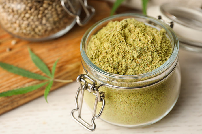Jar of dehydrated green powder with cannabis leaves on a wooden surface